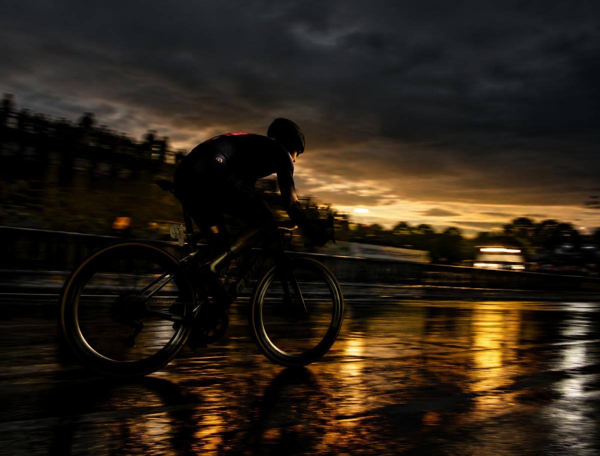 Rennradfahrer in Silhouette auf nasser Strecke in der Abenddämmerung